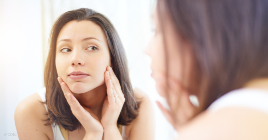 Woman looks in mirror wondering what is a fair price to pay for a BOTOX treatment