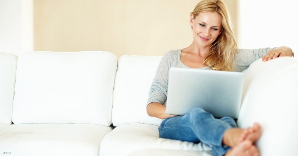 Woman sitting on couch at home reading Koch Facial Plastic Surgery's blog addressing rescheduling after COVID-19